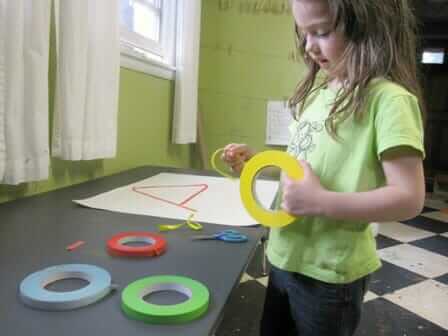 A young girl tearing marking tape to pieces and adhering to paper.