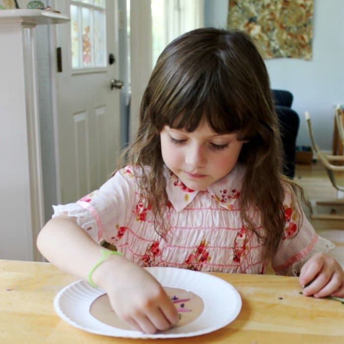 A young girl sticking flower petals to the paper plate frame with contact paper.