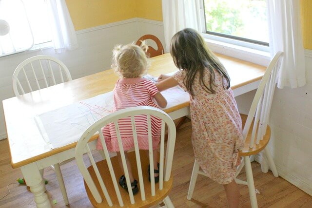 Two young girls scribbling on a sheet of easel roll using oil pastels.