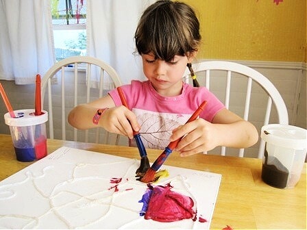 Child painting yarn with two paint brushes