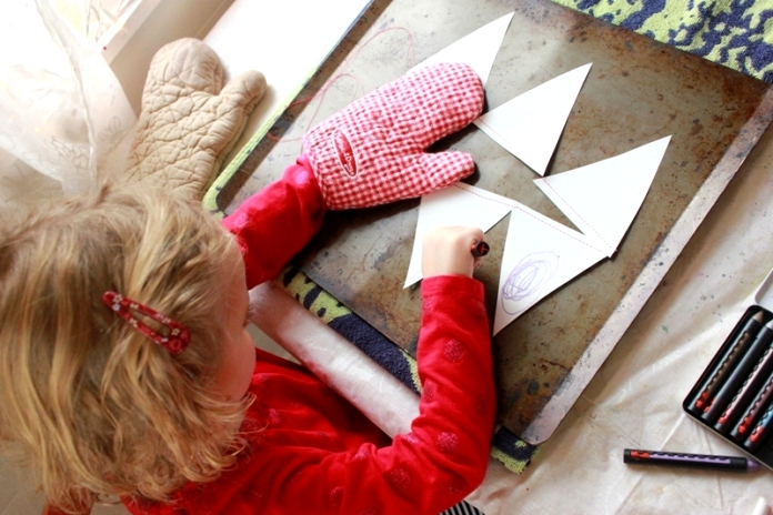 A young girl using crayon to draw on a paper bunting over a heated cookie sheet