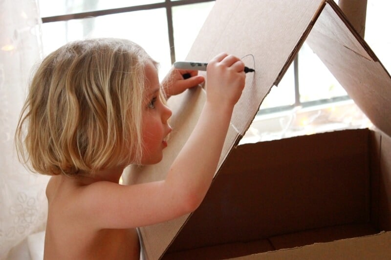 Girl drawing on cardboard dollhouse