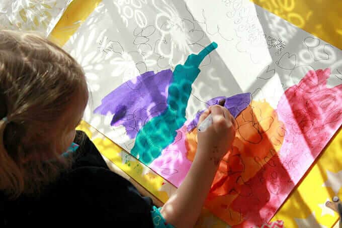 A young girl painting over the shadow coming through a sheer floral curtain.
