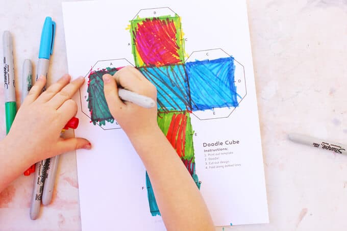 A child drawing colorful lines on the doodle cube pattern.