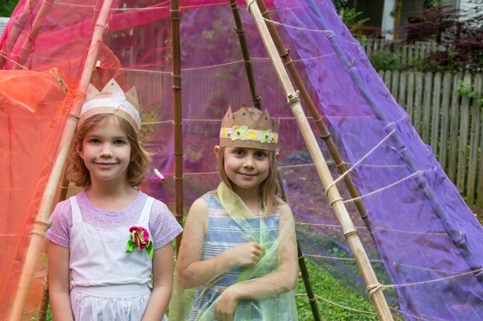 Two kids wearing their new handmade flower crowns and ready for pretend play in a backyard teepee.