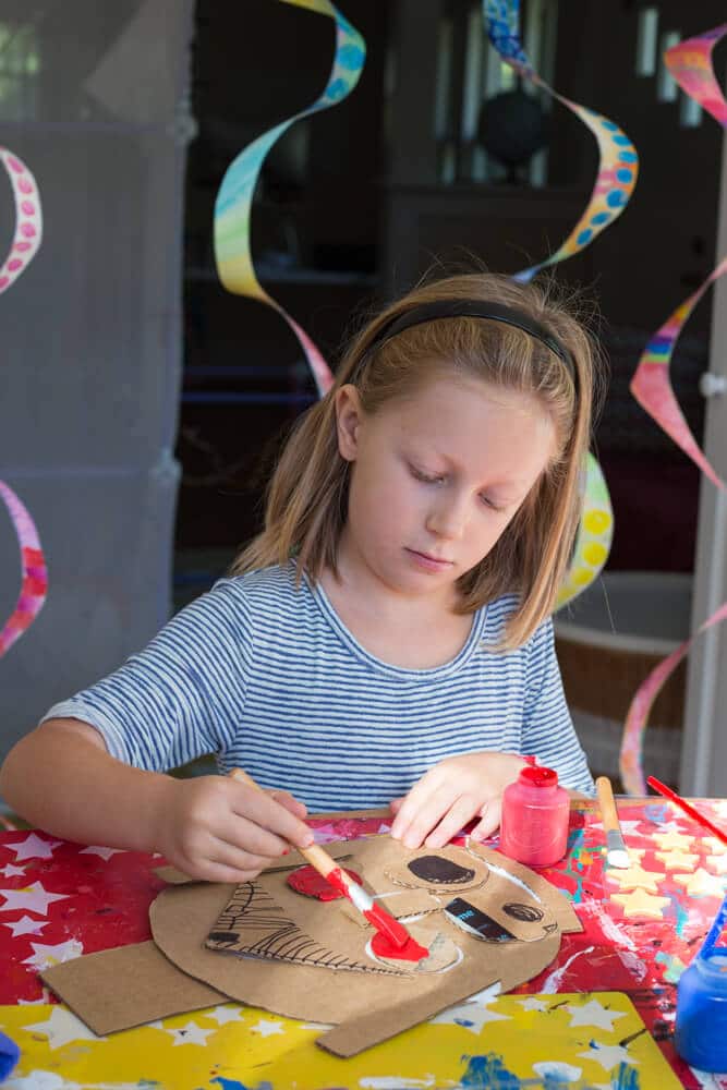 A young girl adding details and painting the cardboard portrait.