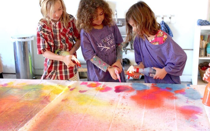 Kids spraying paint for a collaborative mural art project.