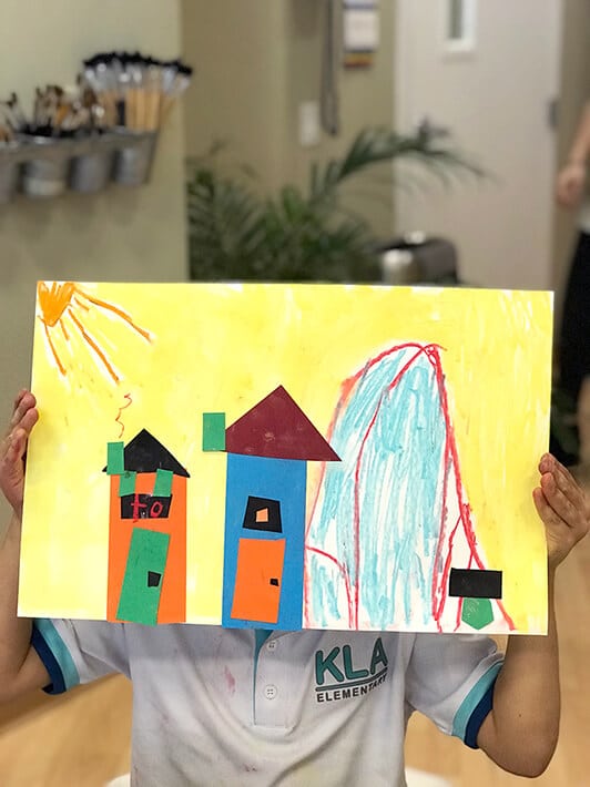 Boy holding up mixed media collage artwork of cities – Paul Klee Art for Kids