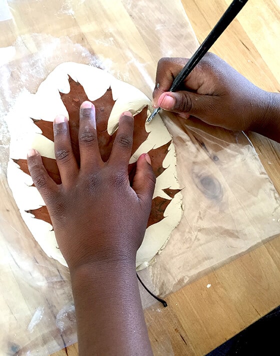 Child creating leaf impression with leaf in clay