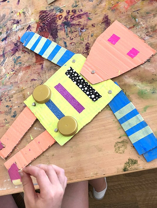 Child making a robot puppet using cardboard, paint & other recycled materials