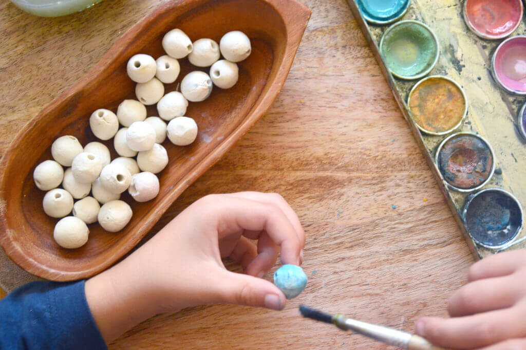 Child painting clay beads for nature mobile