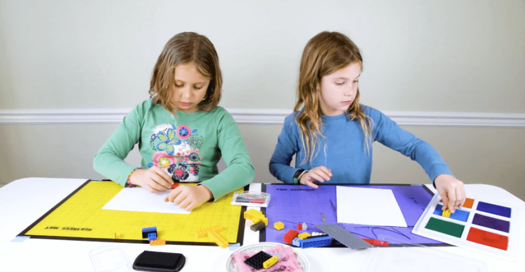 Two girls using stamp pads & LEGOs to create LEGO prints