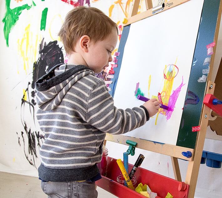 Toddler boy drawing on paper at easel in studio