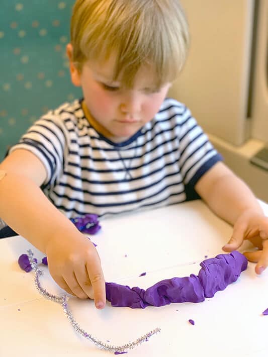 Boy playing with playdough and pipe cleaners, a great open ended art activitiy for traveling with toddlers