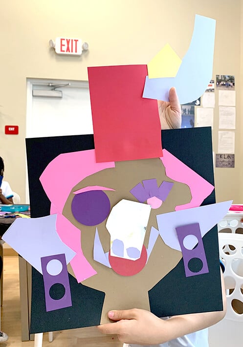 Student holds up Picasso inspired collage portrait with pink and purples cut paper shapes