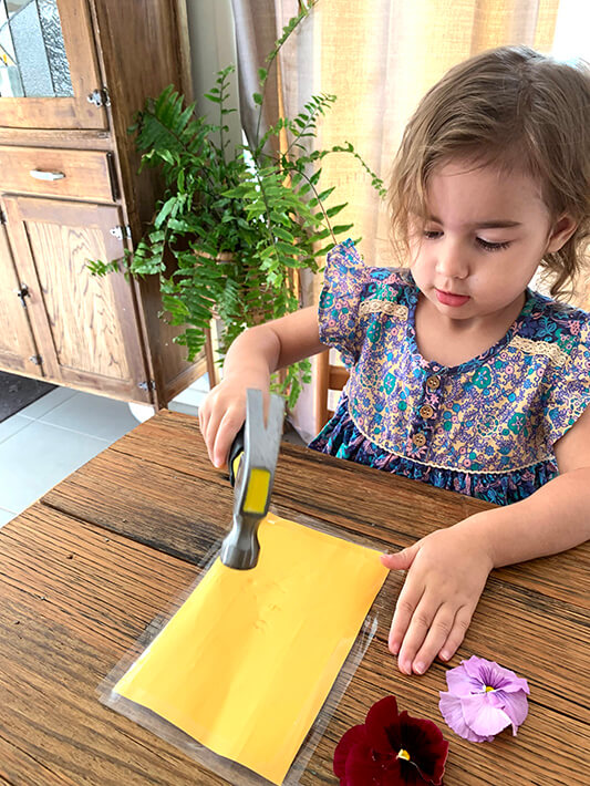 Child flower pounding at table with flowers nearby