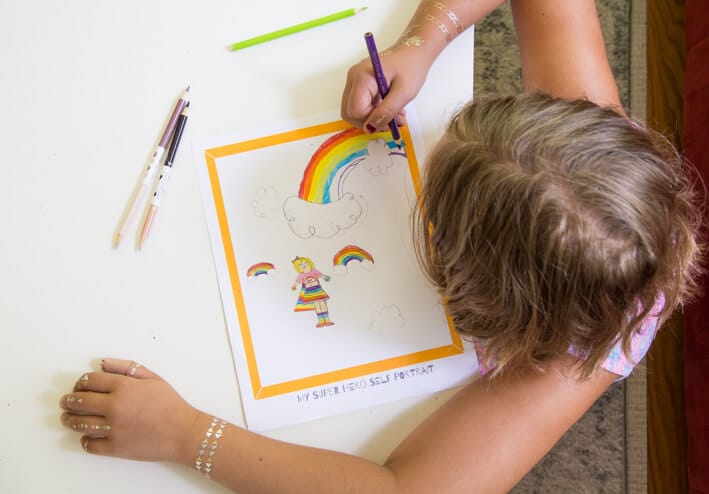 Child drawing her superhero self portrait with rainbow powers