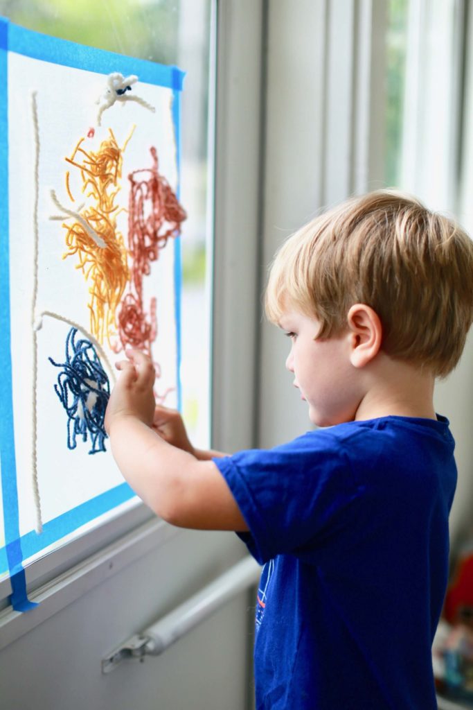 Boy placing yarn on contact paper suncatcher for kids
