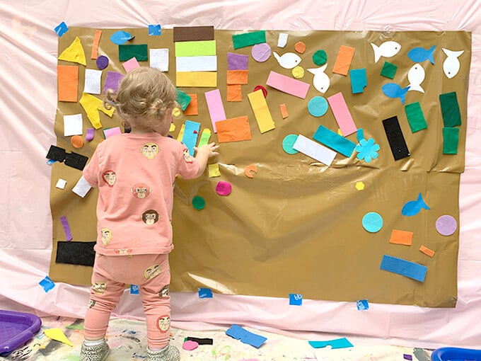 Child placing felt shapes on contact paper wall