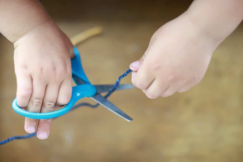 Child cutting blue yarn with scissors
