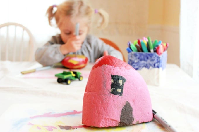 child decorating painted rock house