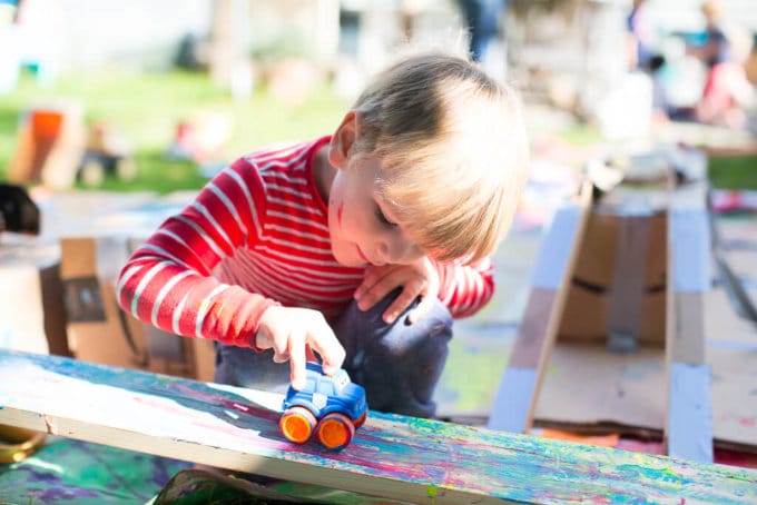 A boy pushing a car on a wooden ramp to make painted tracks