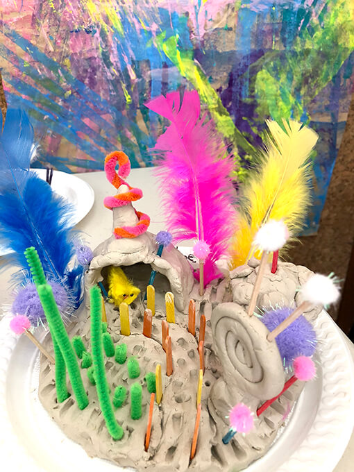 A small world in clay with pipe cleaners, pom poms and mini popsicle sticks
