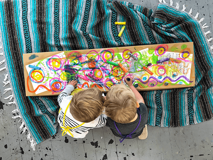 Two children painting with tempera sticks on sheet music