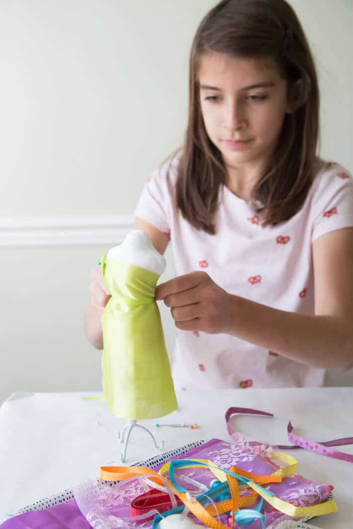 Fashion design for kids with a kit - girl designing a dress on a small mannequin from a craft kit