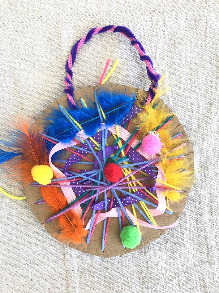 Circular cardboard weaving with yarn, pom poms & feathers