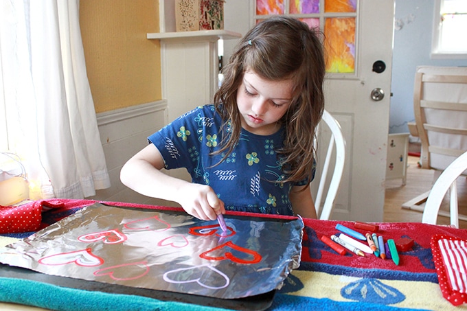Girl drawing with melting crayon on foil