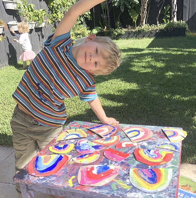 Child standing at table with painted cardboard rainbows