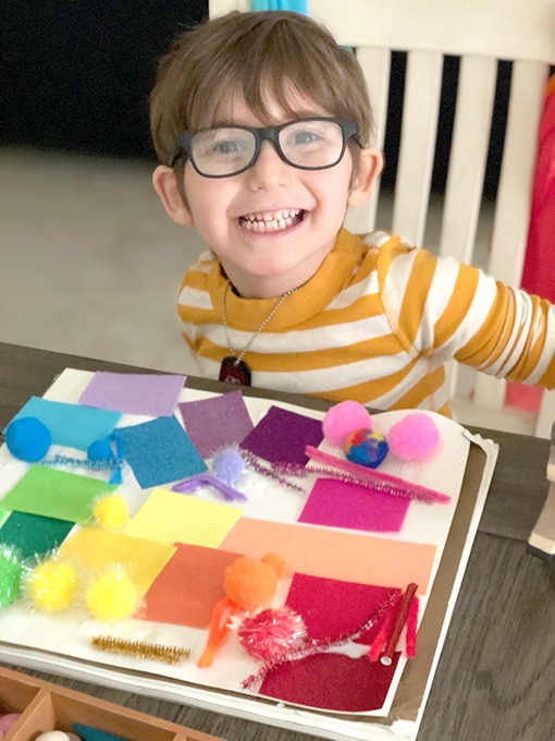 Boy sitting at table with rainbow collage. creative preschool activities