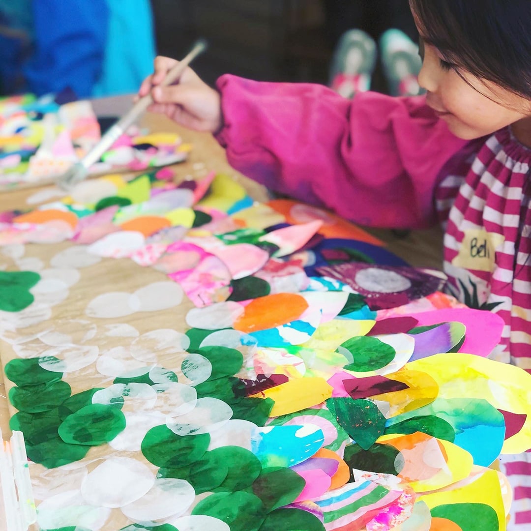 Girl painting paper feathers onto DIY paper wings with glue and paintbrush