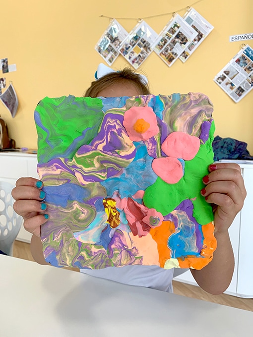 Child holding up painting with clay project