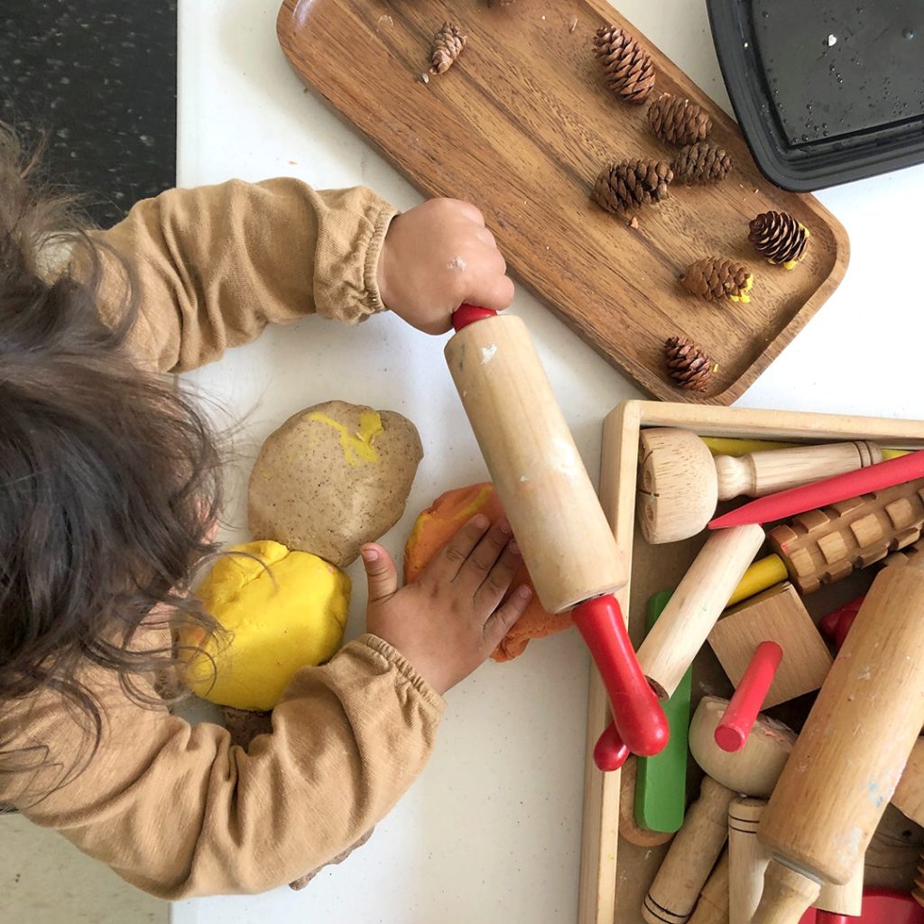 Child patting autumn playdough with playdough tools on table