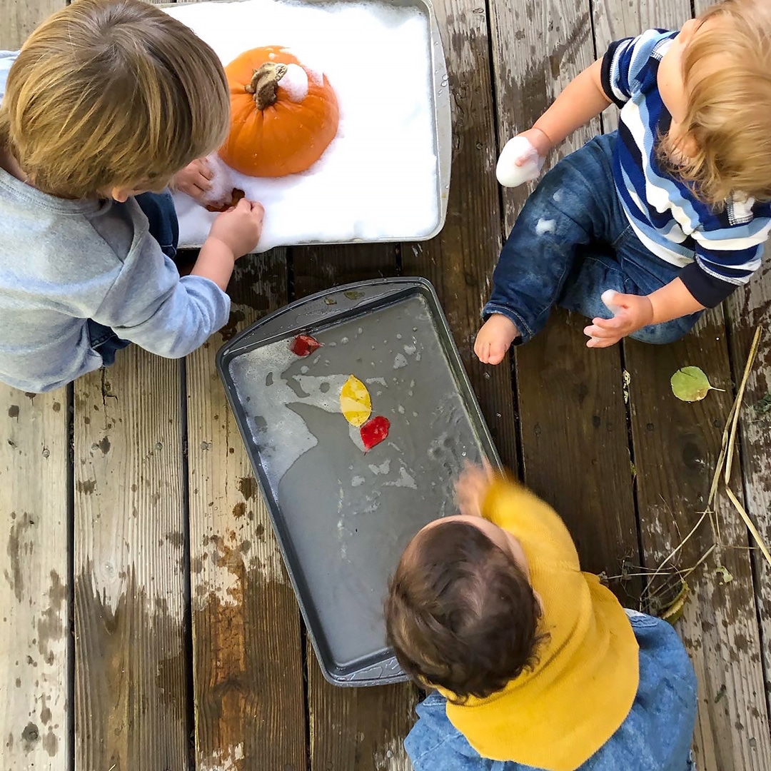 Three kids playing with floating leaves in water and pumpkin in foamy soap – fall sensory play ideas for kids. 