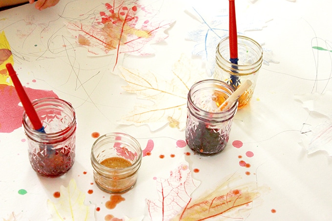 Liquid watercolor paints and brushes in glass jars with wax resist paper leaves