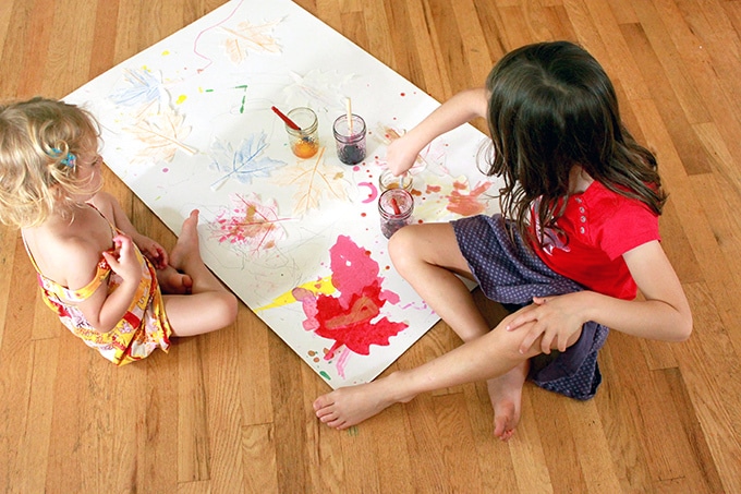 Two girls painting wax resist paper leaves with watercolor paints on the floor
