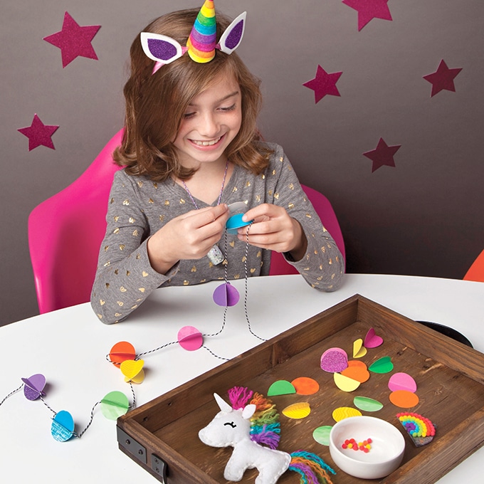 Girl wearing unicorn headband and making a rainbow paper garland with Craft-tastic craft kit