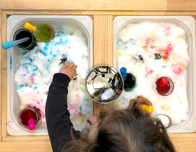 Child painting snow with liquid watercolors and pipettes.
