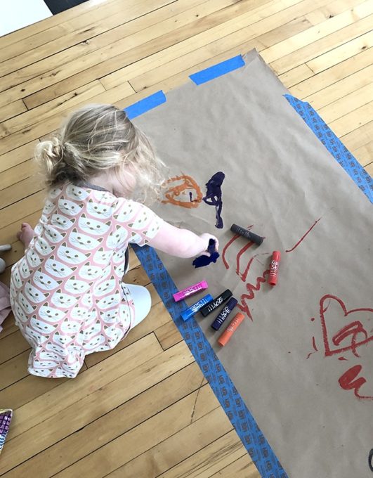 Child painting with kwik stix on large paper on floor-Photo by Andrea Martelle