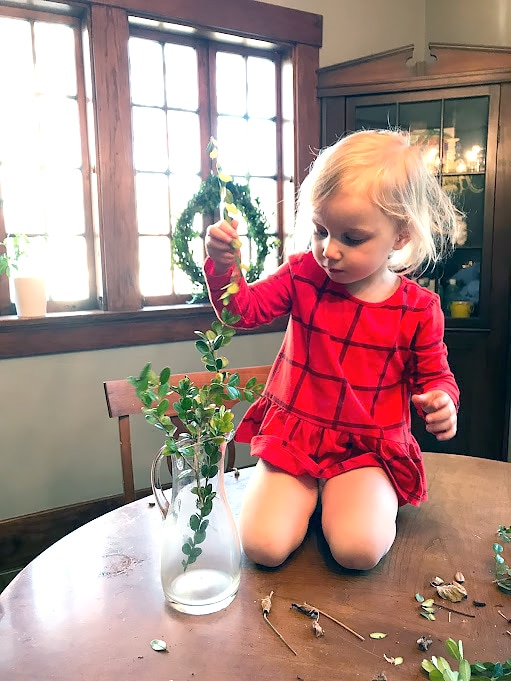 Child placing natural greenery in vase