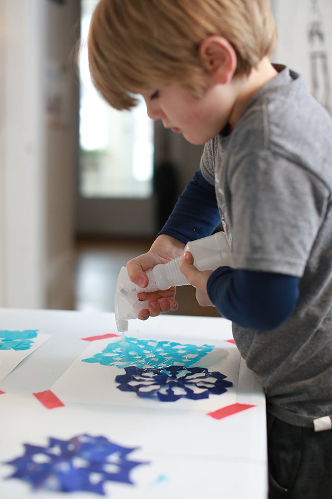 Boy spritzing tissue paper snowflakes