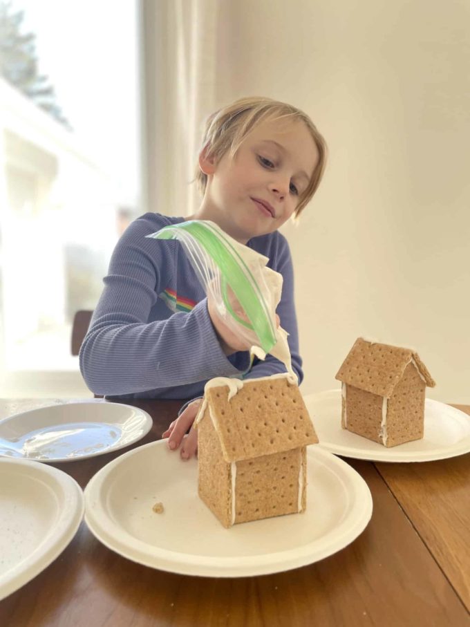 child piping icing on gingerbread house