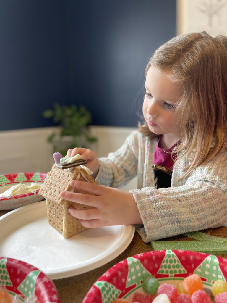 child decorating graham cracker gingerbread house