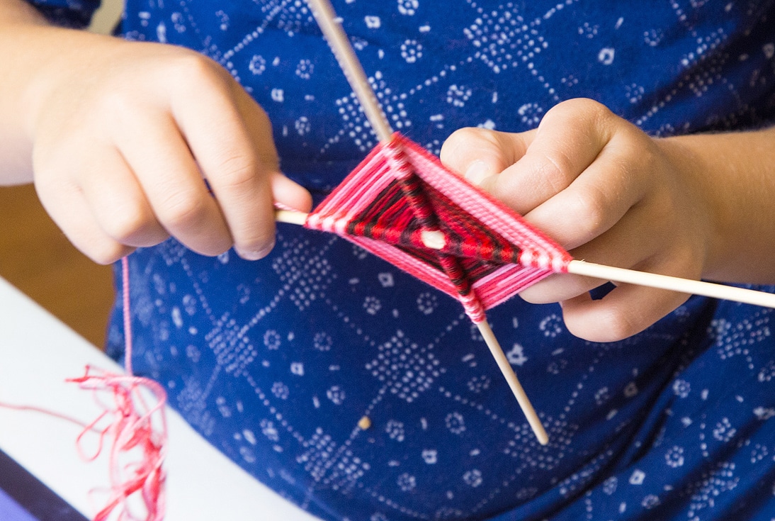 child weaving God's eye craft