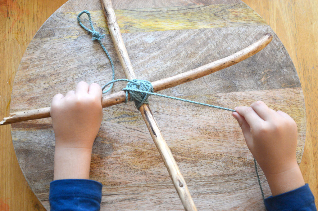 Child winding cord around sticks in x shape for nature mobile