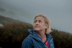 Portrait of a senior woman outdoors in a blue jacket, looking upwards with a thoughtful expression.