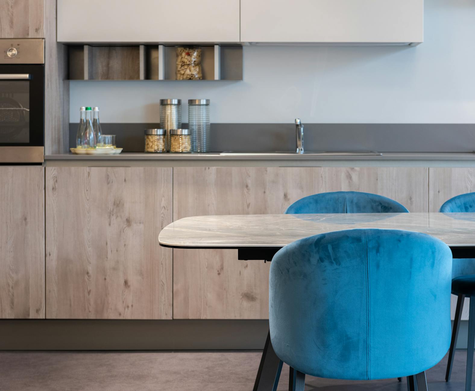 Stylish modern kitchen featuring blue velvet chairs and wooden cabinetry, perfect for contemporary homes.